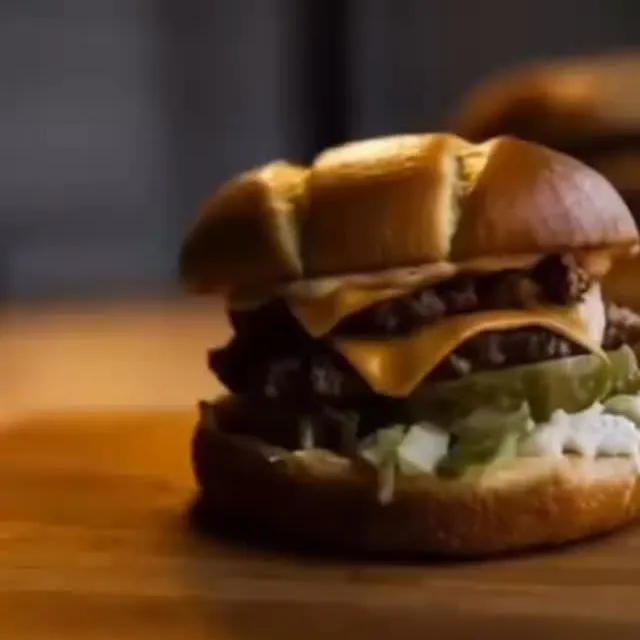 A double smash burger with melted American cheese, pickles and shredded lettuce on a brioche bun, sitting on a wooden board.