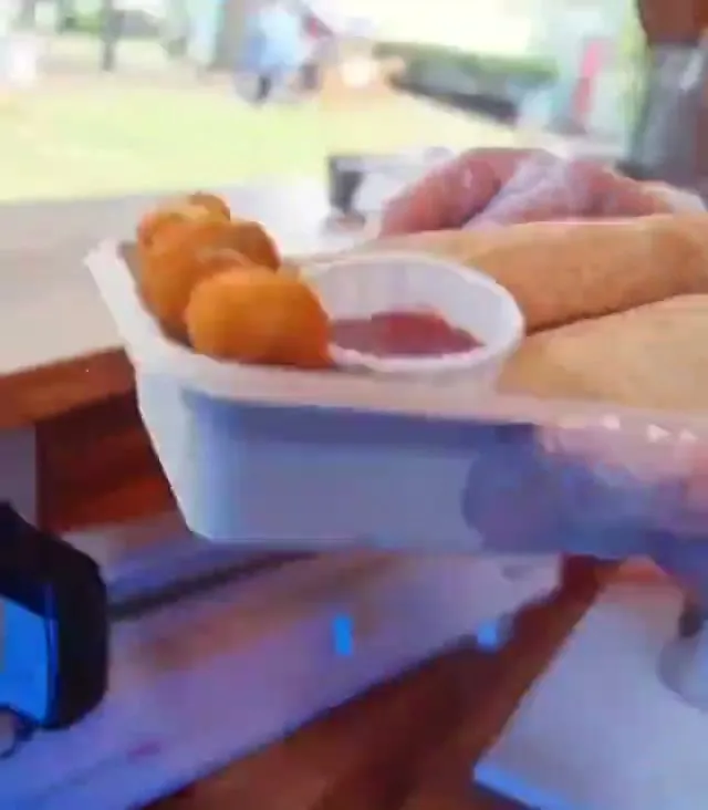 A takeaway box held up outside the truck — a grilled wrap, falafel and a pot of sauce.