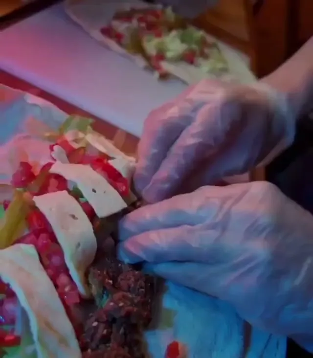 Gloved hands building a shawarma wrap on the truck's prep bench — shaved meat, tomato and salad laid along a flatbread.